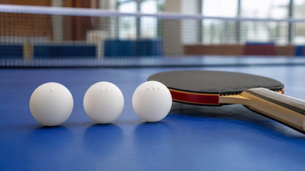 Trois balles de tennis de table représentant les niveaux 1, 2 et 3 étoiles, posées sur une table bleue avec une raquette en arrière-plan.
