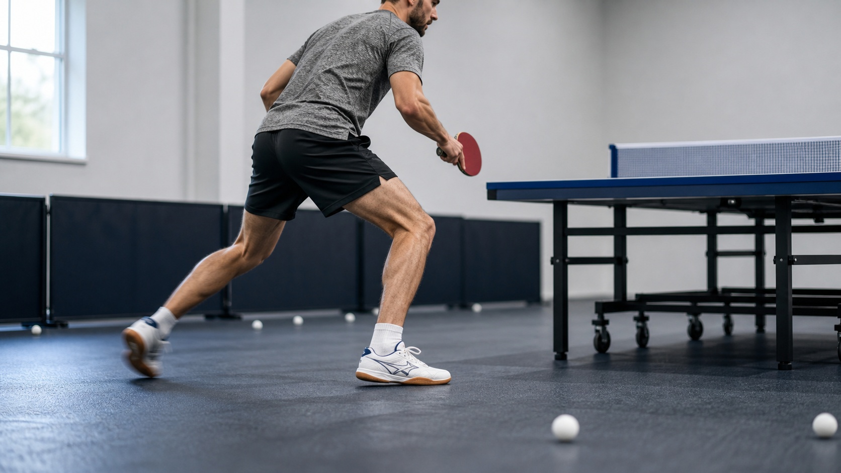 Joueur de tennis de table effectuant un exercice de déplacement latéral, pieds bien placés près de la table.